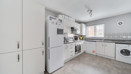 White fitted kitchen with appliances, cabinets and a window letting in daylight.