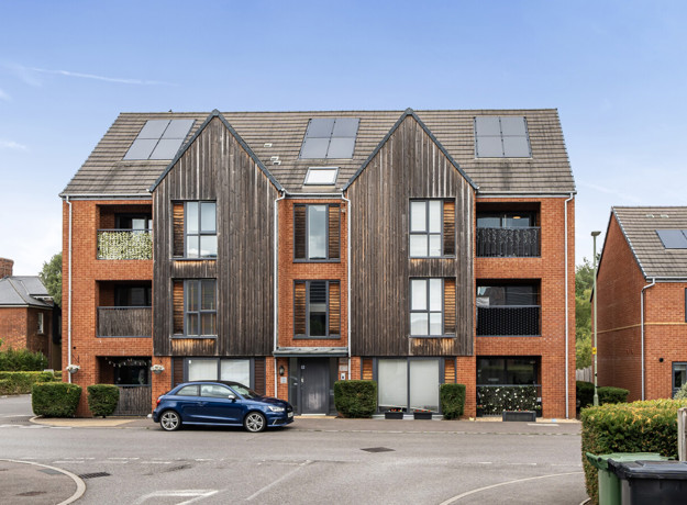 Exterior view of a red brick apartment building with parked cars outside.