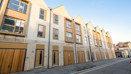 Row of modern townhouses along a clean street with pale brick and large windows.