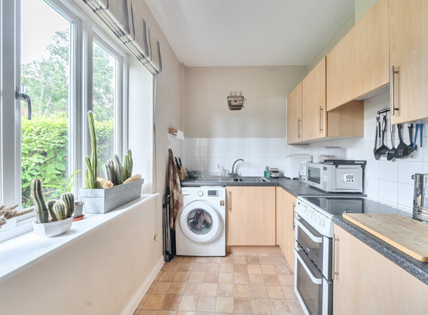 Kitchen with wooden-effect cabinets, dark worktops, sink, appliances, and window.