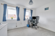 Room with desk, office chair, desktop screen and two windows with curtains.