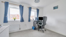 Room with desk, office chair, desktop screen and two windows with curtains.