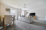 Living room with grey carpet, sofa, TV, dining table and garden doors.