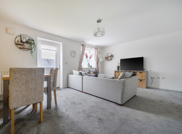 Living room with grey carpet, sofa, TV, dining table and garden doors.