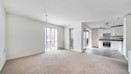 Open-plan living area with carpeted floor and kitchen in the background. (1)