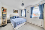 Bedroom with double bed, shelving unit and windows with curtains.