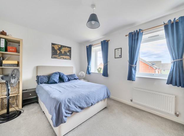Bedroom with double bed, shelving unit and windows with curtains.