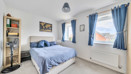 Bedroom with double bed, shelving unit and windows with curtains.