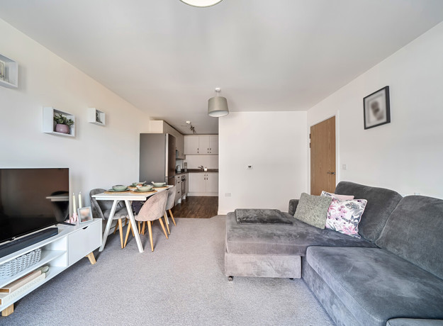 Living room with corner sofa, television and dining area leading to a kitchen.