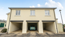 Coach house with cream exterior and three open garages on a paved driveway.