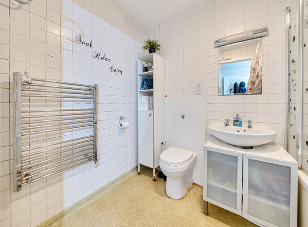 Bathroom with tiled walls, bathtub, toilet, sink unit and wall-mounted towel rail