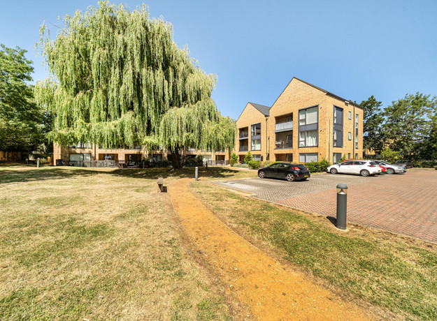 Apartment building with parking spaces, a lawn, and a footpath.
