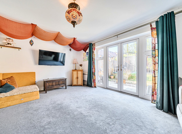 Living room with carpet, sofa, wall-mounted television and patio doors.