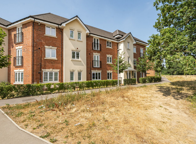 Three-storey brick apartment building with grass and trees in front.