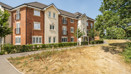 Three-storey brick apartment building with grass and trees in front.