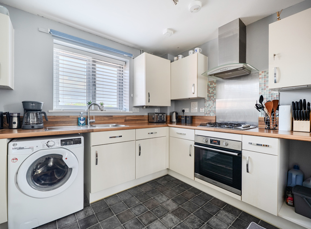 Kitchen with white cabinets, washing machine, and wood effect countertop.