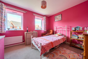 Bright pink bedroom with single bed, shelving, desk and window providing natural light