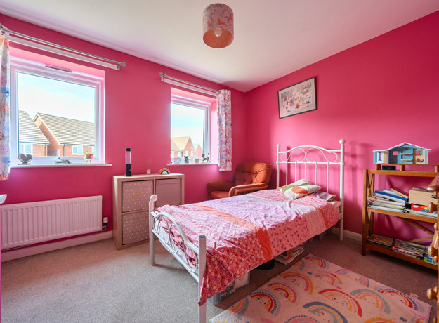 Bright pink bedroom with single bed, shelving, desk and window providing natural light