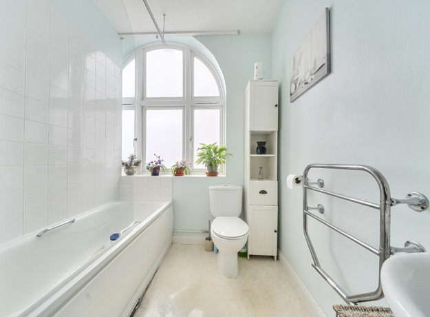 Bathroom with bathtub, toilet, sink, towel rail, and tiled walls with window.
