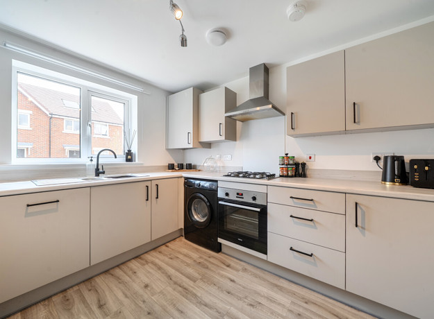 Modern kitchen with white cabinets, light coloured worktops, integrated appliances and window.