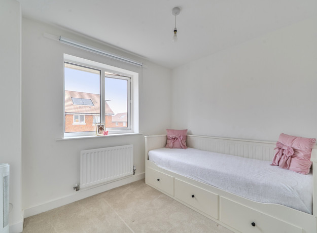 Second bedroom with single bed, white walls, window, and radiator below sill.