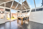 Conservatory with glass roof, tiled floor, and wooden dining table with chairs.