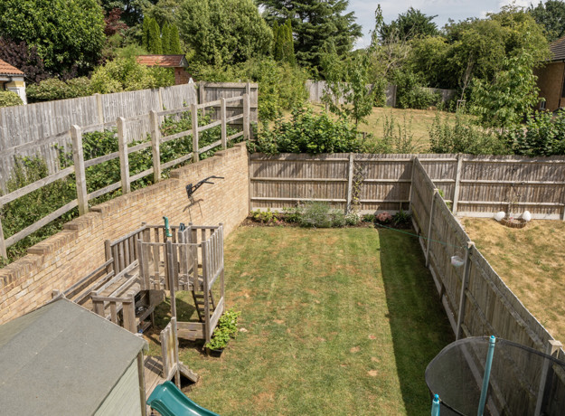 Elevated view of a fenced rear garden with grass and patio areas.