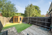 Rear garden with decking, lawn, trees, and wooden outbuilding.