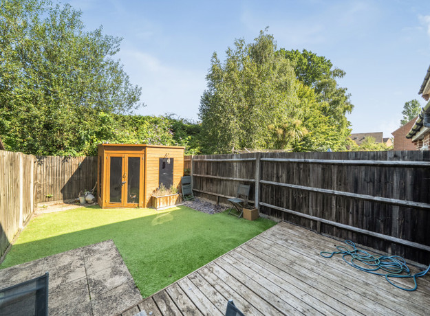 Rear garden with decking, lawn, trees, and wooden outbuilding.