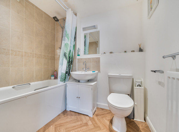 Modern bathroom featuring a bath with shower attachment, wash basin, toilet, and tiled walls.
