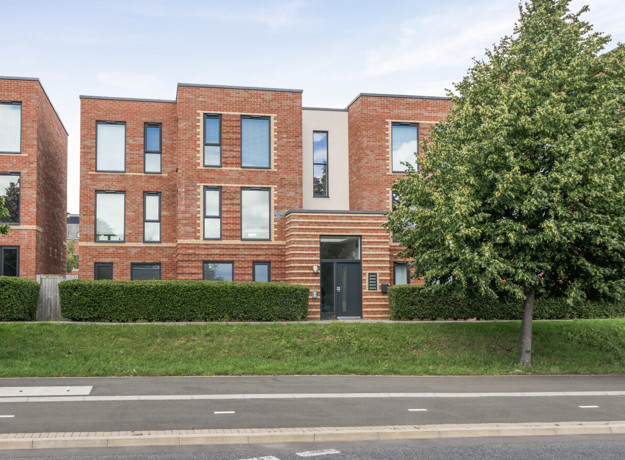 Apartment building with landscaped grounds and a tree beside the entrance.