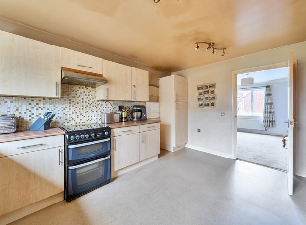 Kitchen with wooden cabinets, tiled floor, and freestanding cooker near a internal door.