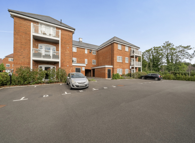 Apartment block with parking spaces, brick facade, and surrounding trees.