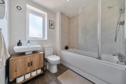 Bathroom with bathtub, shower screen, sink unit, toilet, and frosted window.