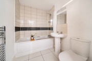 Bathroom with a bathtub, pedestal sink, toilet, and tiled walls.