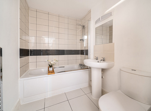 Bathroom with a bathtub, pedestal sink, toilet, and tiled walls.