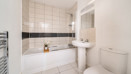 Bathroom with a bathtub, pedestal sink, toilet, and tiled walls.