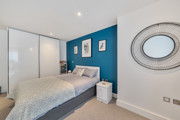 Bedroom with double bed, blue feature wall, wardrobe with sliding doors and mirror on the wall.