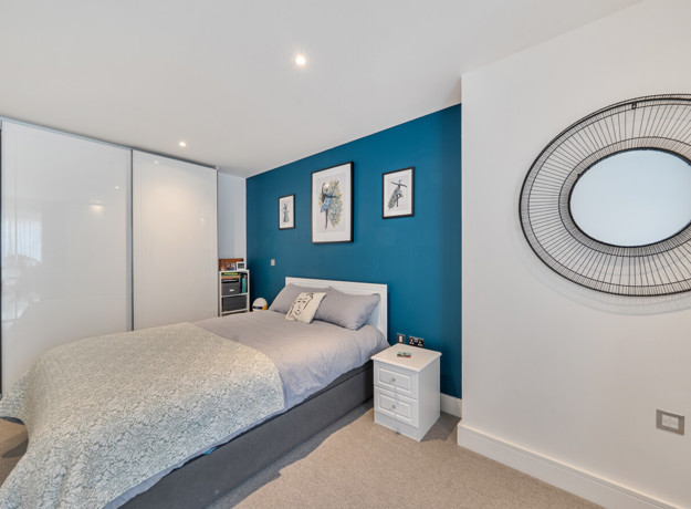 Bedroom with double bed, blue feature wall, wardrobe with sliding doors and mirror on the wall.