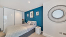 Bedroom with double bed, blue feature wall, wardrobe with sliding doors and mirror on the wall.