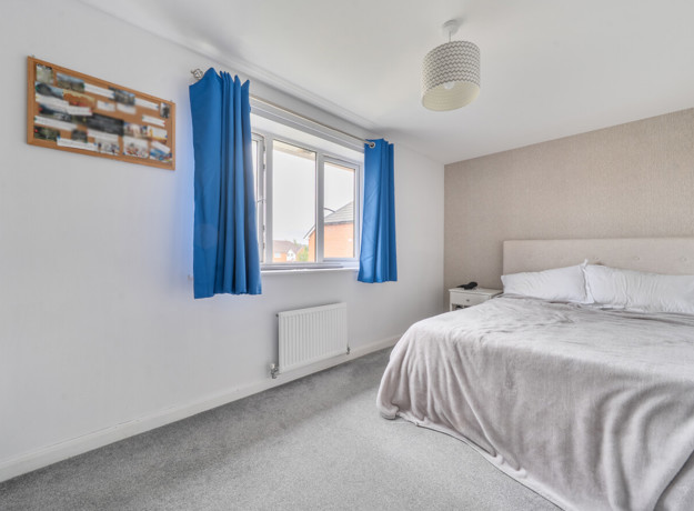 Bedroom with bed, window, radiator and light coloured walls.