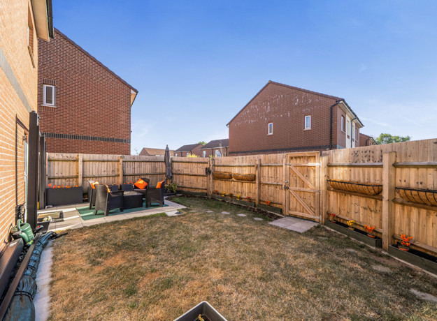 Fenced rear garden with patio area with seating and grass lawn.