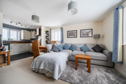 Open plan living room with grey sofa bed, small table, and kitchen in background.