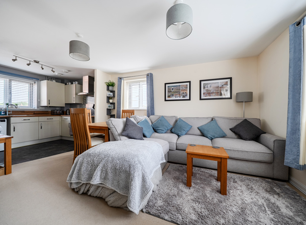 Open plan living room with grey sofa bed, small table, and kitchen in background.