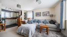 Open plan living room with grey sofa bed, small table, and kitchen in background.