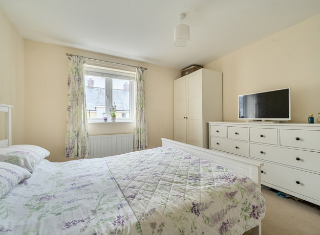 Bedroom with double bed, wardrobe, dresser, TV and window with curtains.