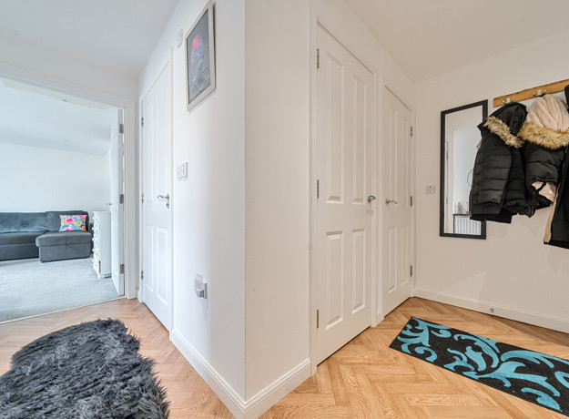 Entrance hallway with wood-effect flooring, storage cupboards, coat hooks, and a view towards the living room.