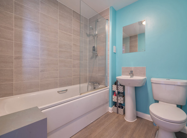 Family bathroom with bath and overhead shower, toilet, sink and tiled walls
