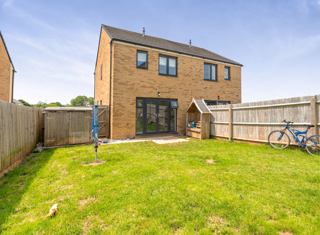 Rear garden with lawn, fenced boundaries, and patio area.