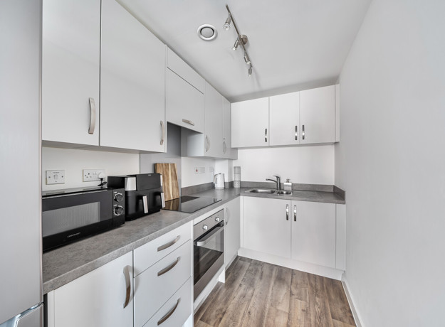 White fitted kitchen with integrated oven, worktops and storage cupboards.